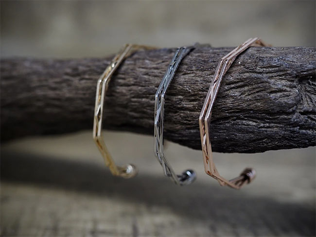 Three geometric cuff bracelets hang on a decorative tree branch