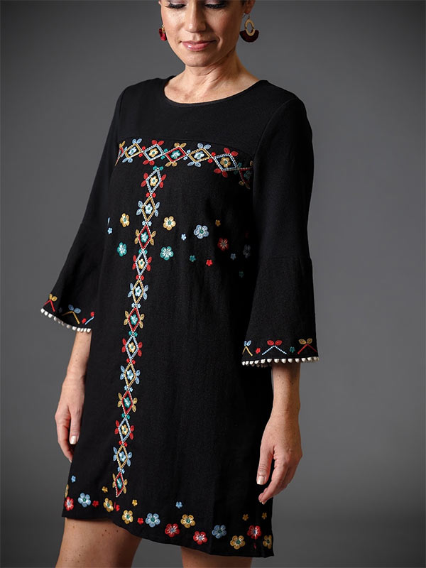 A woman models a black sweater dress as a casual holiday party outfit.