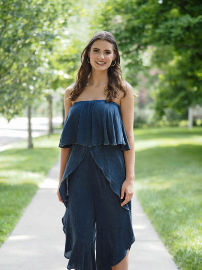 A woman models a strapless denim jumpsuit while standing in a grassy quad.