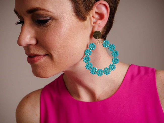 A woman models blue, flower hoop earrings as a jewelry gift idea.