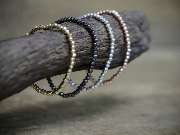 Thin, beaded bracelets hang on a wooden log.