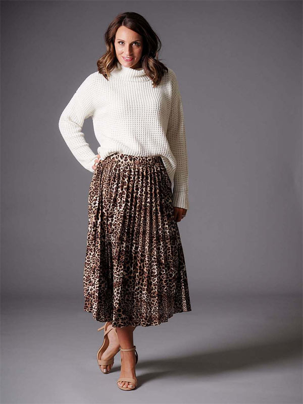 A woman models a leopard print midi-skirt and white sweater as a casual holiday party outfit