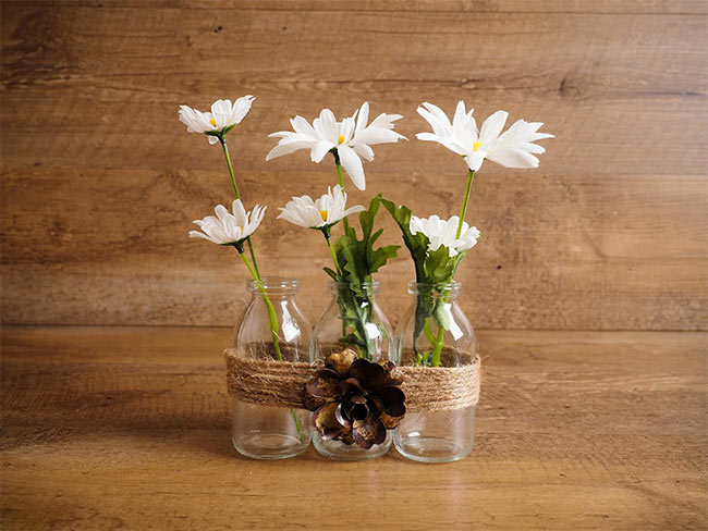 Old glass milk jars wrapped in twine and stuffed with white flowers used as farmhouse home decor