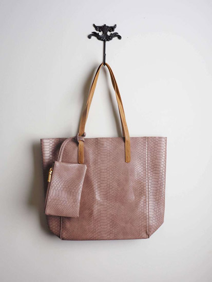 A pink, pastel, faux snakeskin purse hangs on a wall hook.