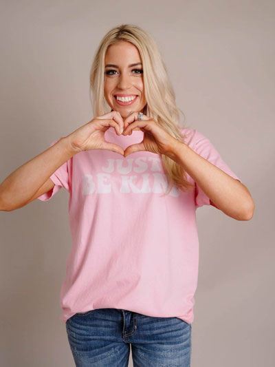 A woman in a pink tee holds her hands in the shape of a heart