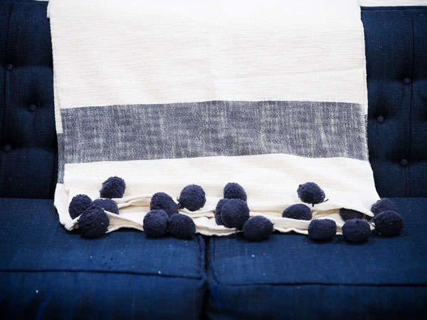  A blanket with pom-pom edges sits on a couch as an example of popular home decor trends in 2020.
