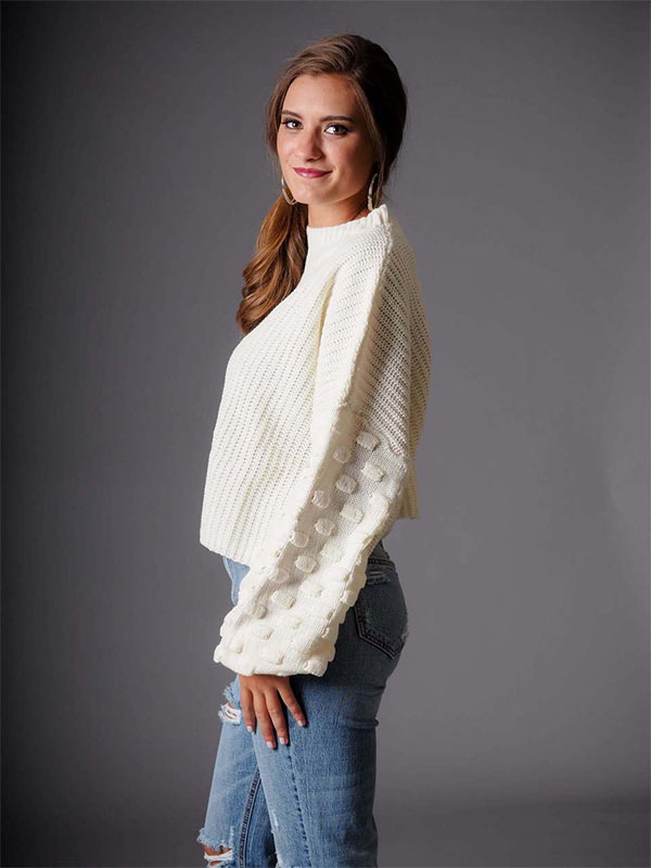 A woman models white, wide-sleeved sweater and jeans as a casual holiday party outfit