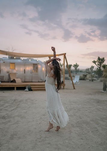 A woman sporting modern hippie style dances barefoot in the sand. 