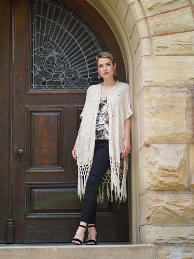 A woman stands in a stone doorway and models a graphic t-shirt under a white cardigan