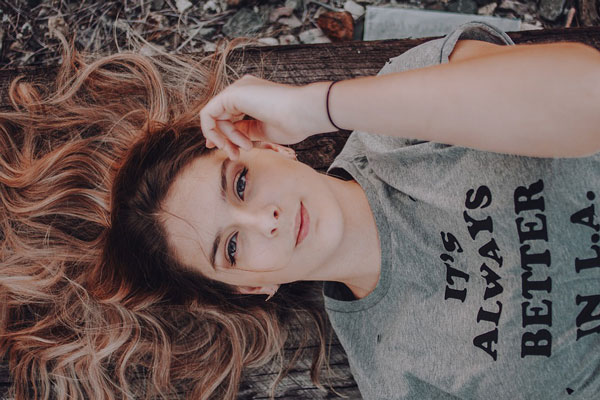 A woman modeling a gray graphic top lies down on the forest floor.