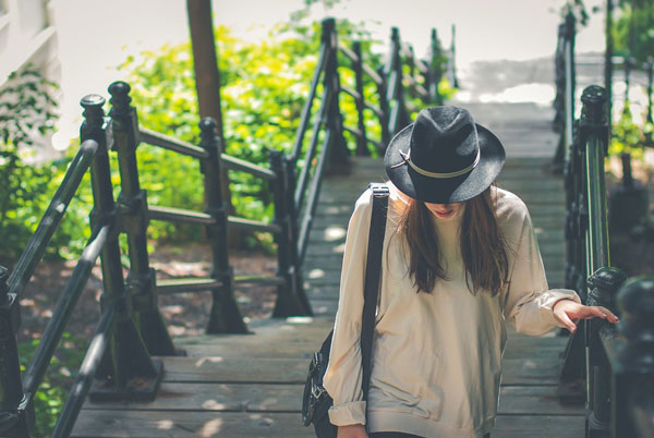 A woman in a hat walks up a flight of outdoor stairs.