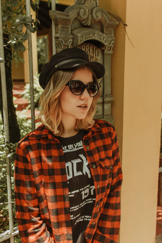 A woman in a black hat demonstrates how to style graphic tees with plaid.