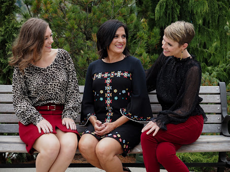 Women in casual holiday party outfits sit and chat on a park bench